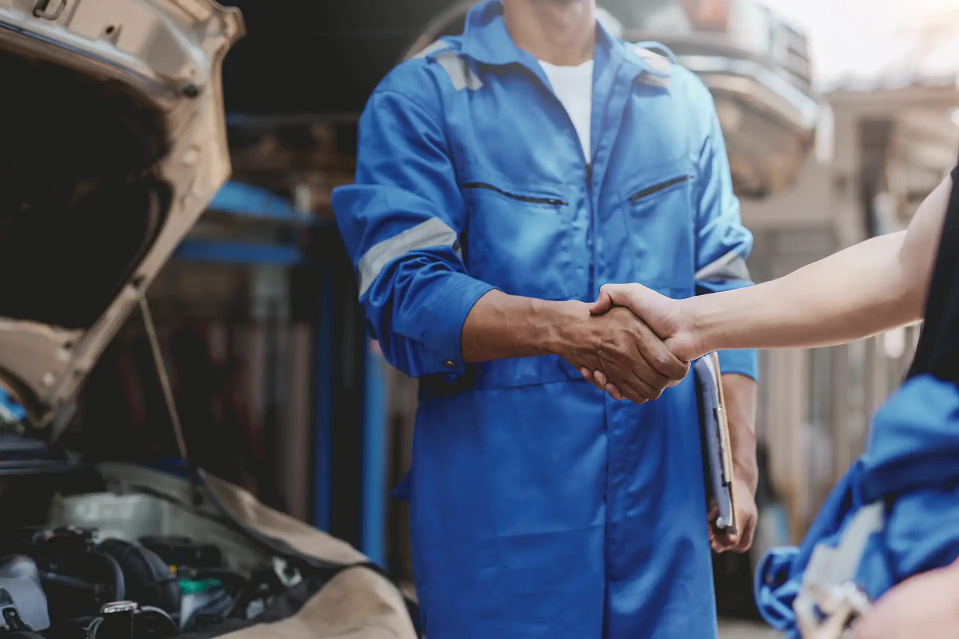 Mécanicien en combinaison bleue serrant la main d'un client dans un garage automobile